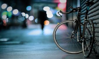 Photo of a bike on a sidewalk, leaning on a garage door, at night with a blurred street background. 