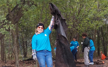 A volunteer holding up a large piece of trash in a wooded area.