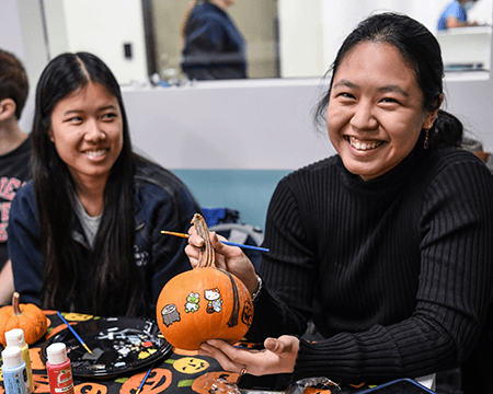 Two smiling people painting designs on small pumpkins.