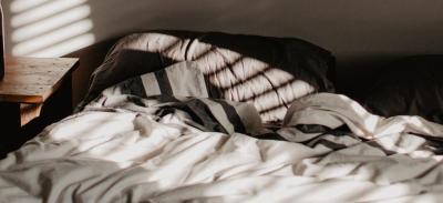 An unmade bed with a sunbeam from an open window shining onto a pillow.