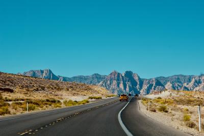 Car driving toward mountains on an empty road.