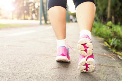 Close up photo of feet wearing tennis shoes, walking on a sidewalk.