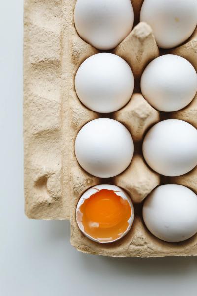 Photo of eggs in an open egg carton with one broken showing the yellow yolk.  