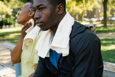 Two men sit outside in the heat, wearing towels around their neck to wipe their sweat. 
