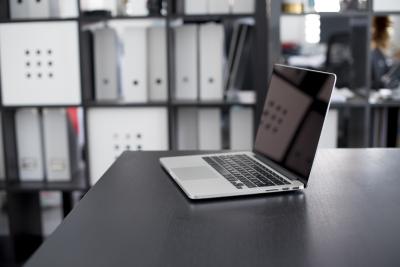 A photo of an open laptop on a table in a file room with full shelves behind the laptop. 
