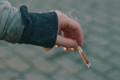 A close up photo of a hand holding a burning cigarette.
