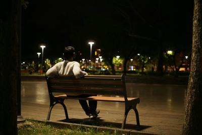 Photo of a man sitting on a bench overlooking a cityscape at night.