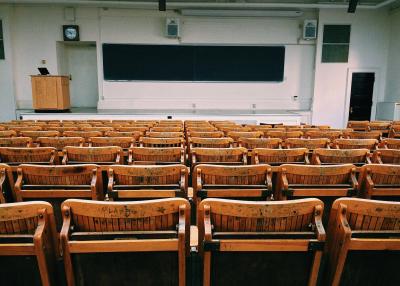 A photo of an empty college, auditorium style classroom with wooden chairs. 