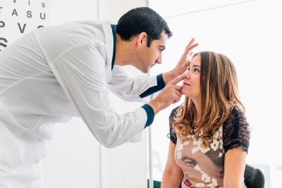 A patient sits while a doctor performs an eye exam.