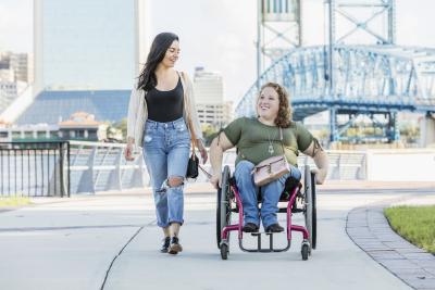 two women on a sidewalk, one in a wheelchair