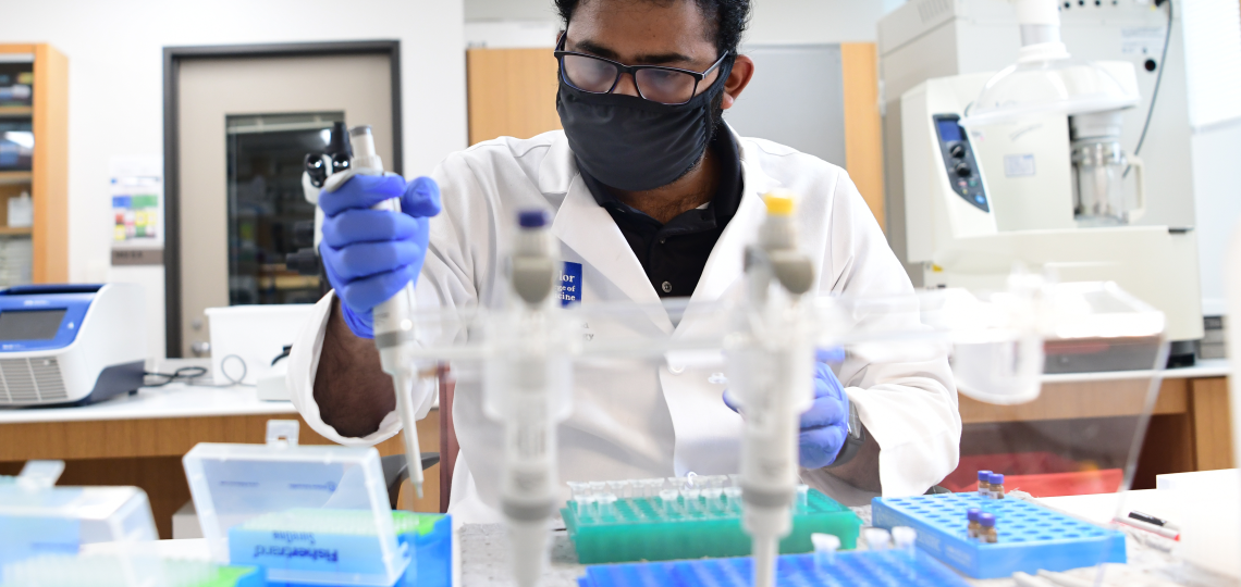 A researcher wearing a face mask works in a lab.