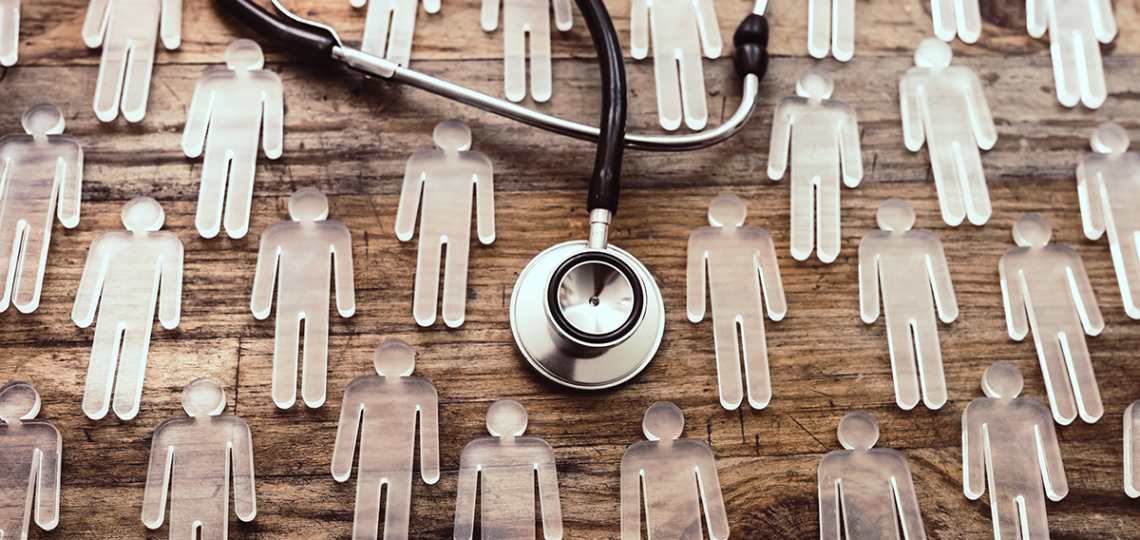 A series of person-shaped plastic cutouts lay among a stethoscope on a wood surface.