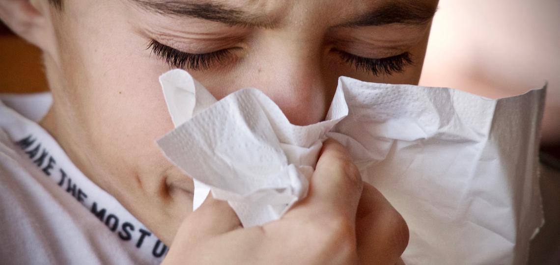 Image of a young boy sneezing into a tissue.