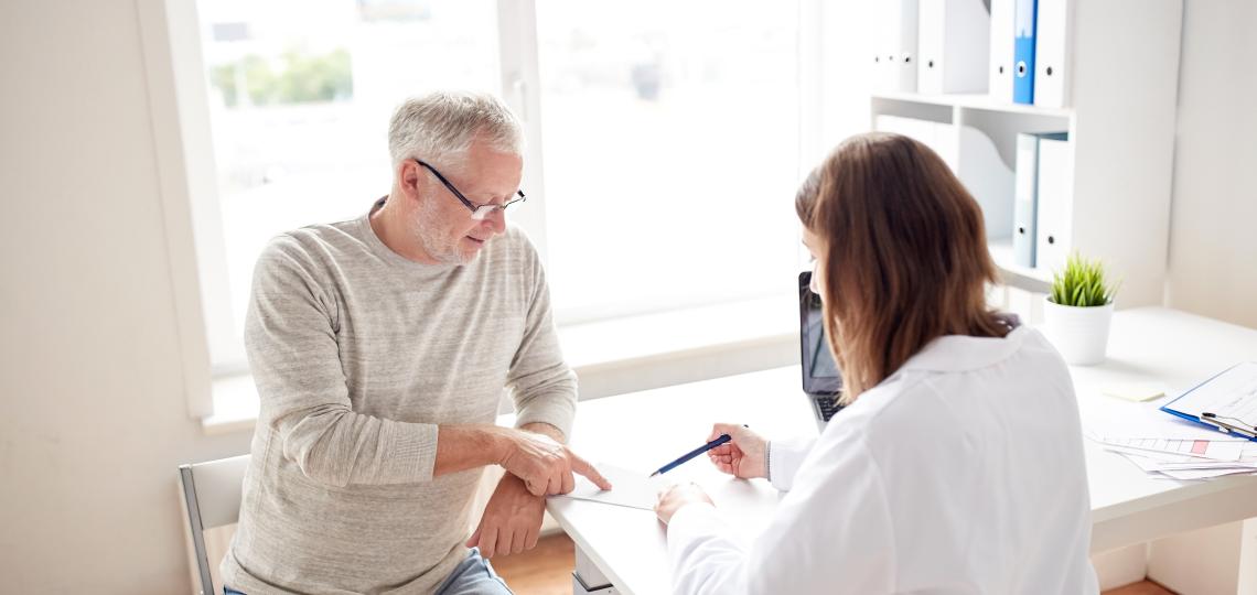 Image of a female doctor with her back to the camera going over a form with an elderly man.