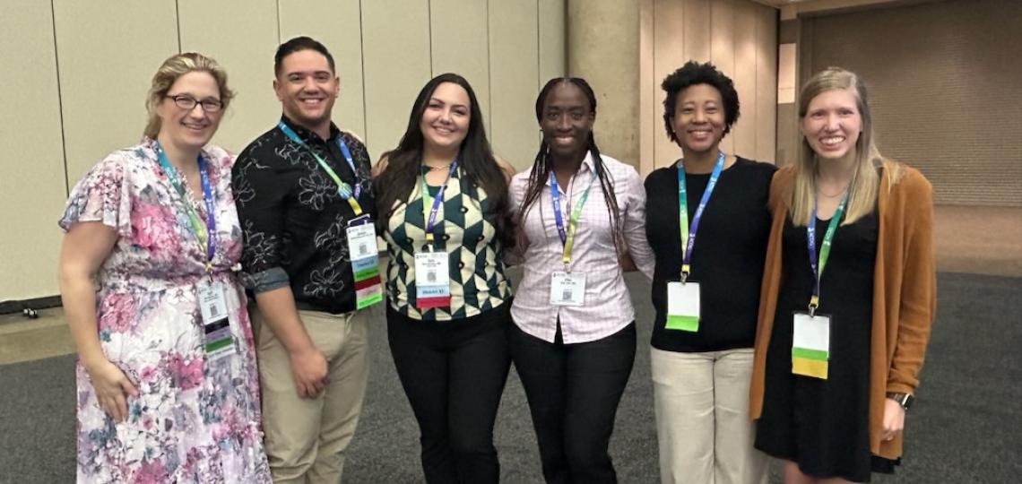 Six people posed in a large room at a conference 