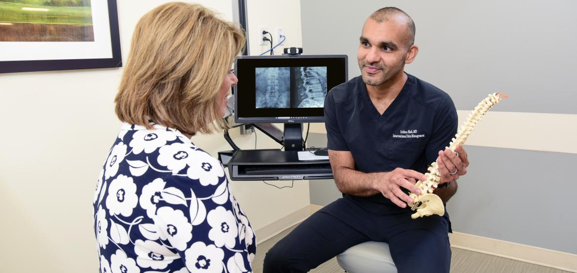 A male physician using a model of a spine to consult a female patient.