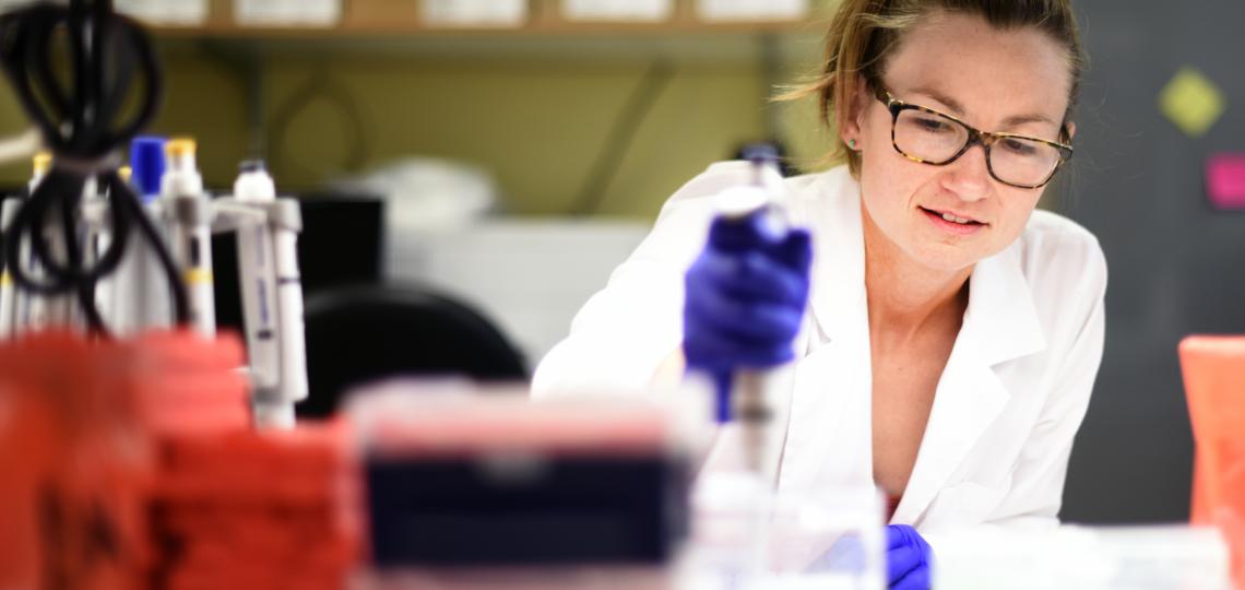 A person in a lab reaching across a desk while handling a sample.