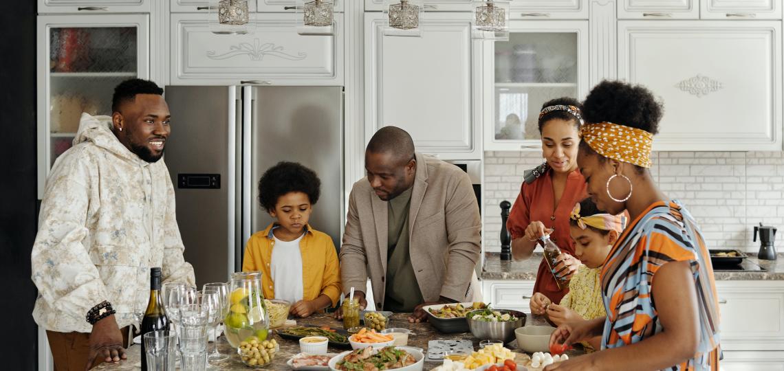 Photo of a family surrounding a kitchen island covered in food. 