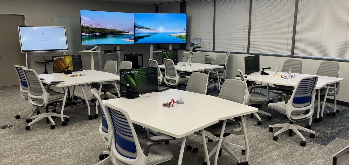 classroom set up with desks, big screens, and a white board