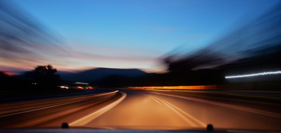 Photo taken at night from the drivers seat of a car of the road with blurred edges to signify driving and movement. 