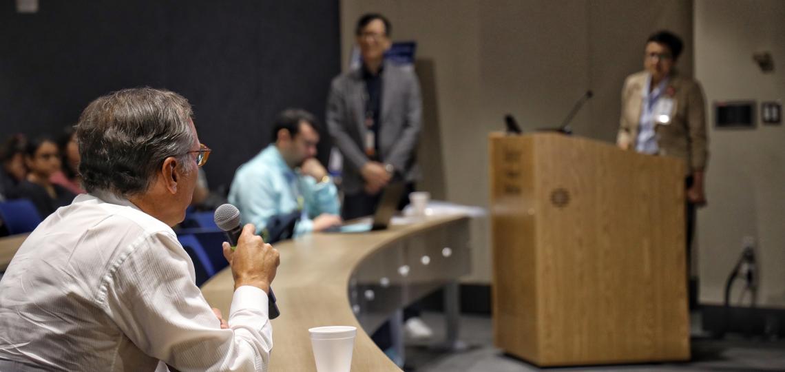 man speaking into microphone towards person at podium