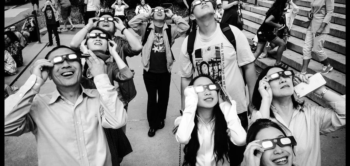 Photo of a group of people wearing solar eclipse glasses looking up at the sky.