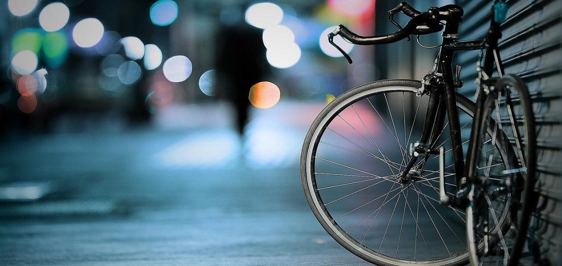 Photo of a bike on a sidewalk, leaning on a garage door, at night with a blurred street background. 