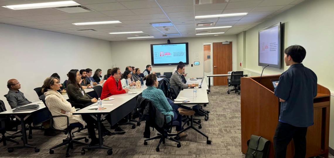 business casual dressed person speaking to a room of people sitting at desks