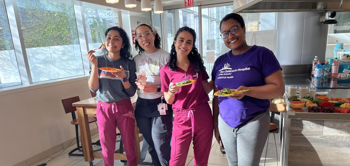 4 women standing in front of bowls of food smiling