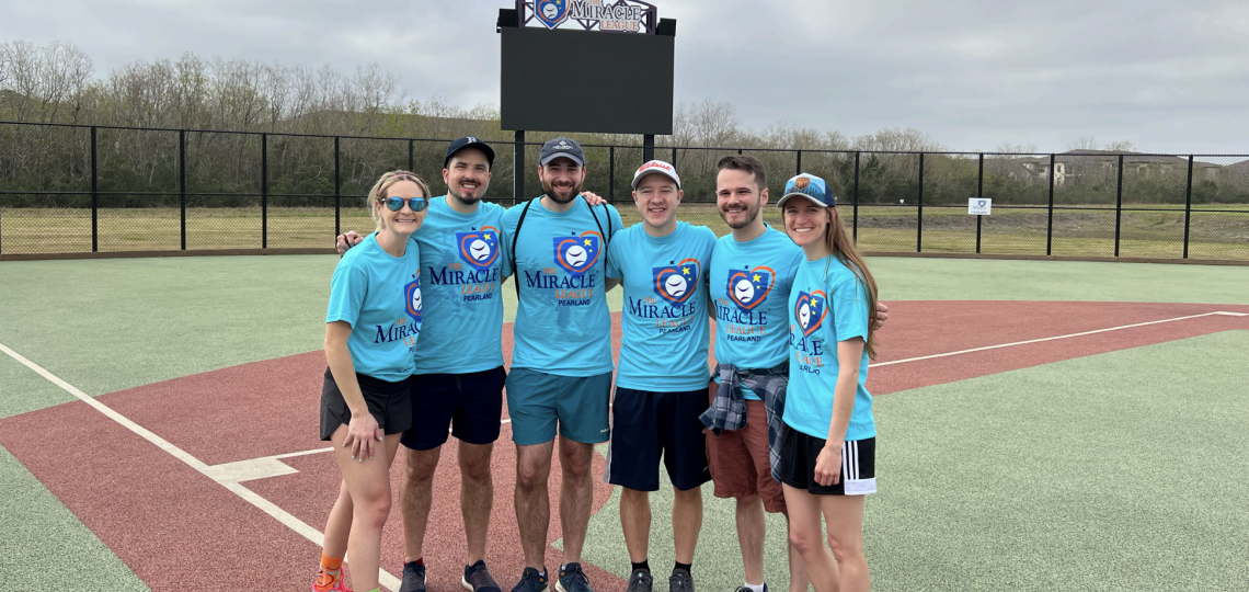 group of people smiling in matching tshirts on a baseball field