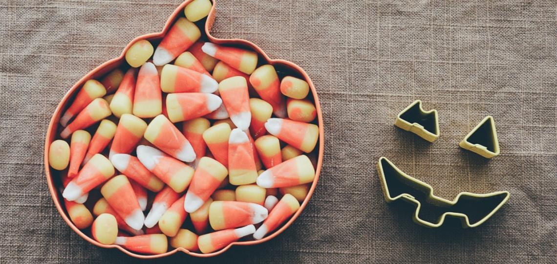 Photo of candy corn in a bowl shaped like an pumpkin. 