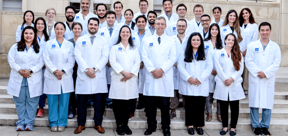 30 people in white coats standing on steps for a group picture.