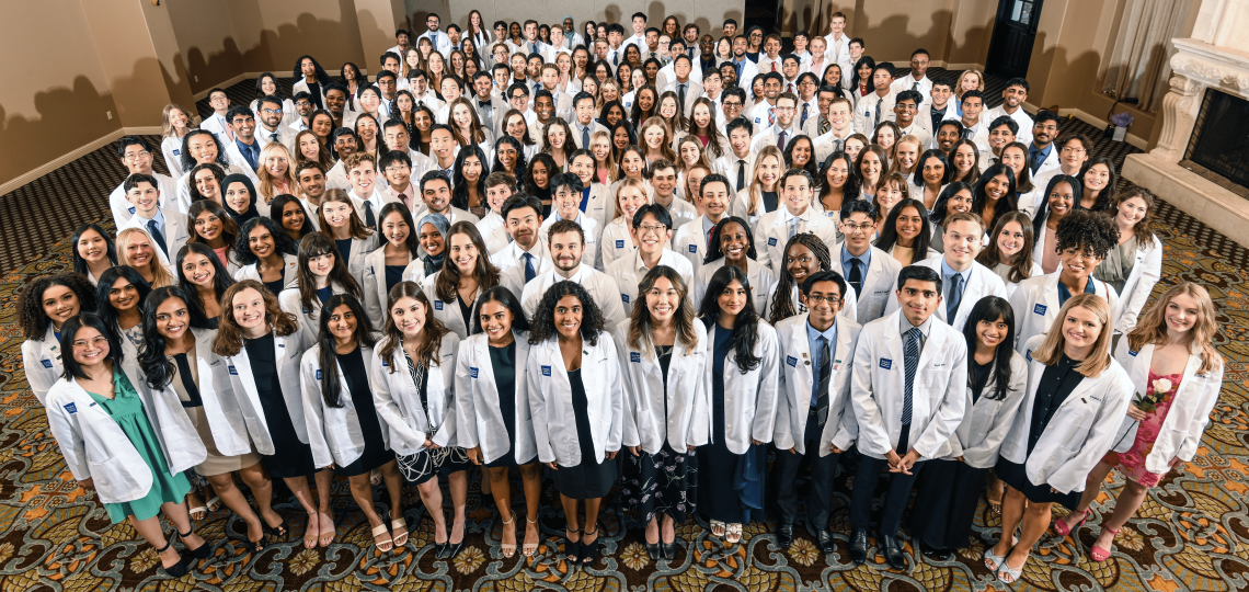 A large group of students seen from above, smiling and proud in their new white coats.