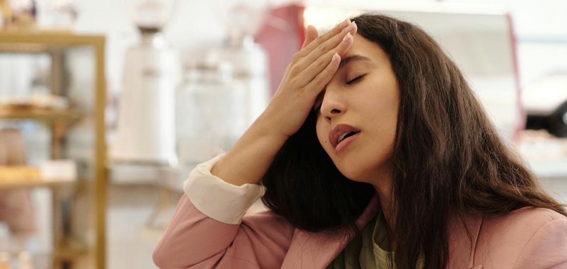 A woman is sitting at work with her hand on her forehead and eyes closed, she is coming down with a cold.