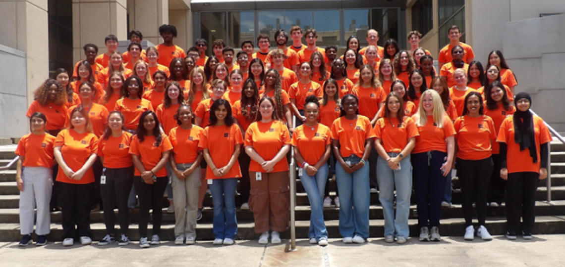 A large group of students wearing matching orange shirts with the Baylor logo. They're smiling, standing in rows on stairs.
