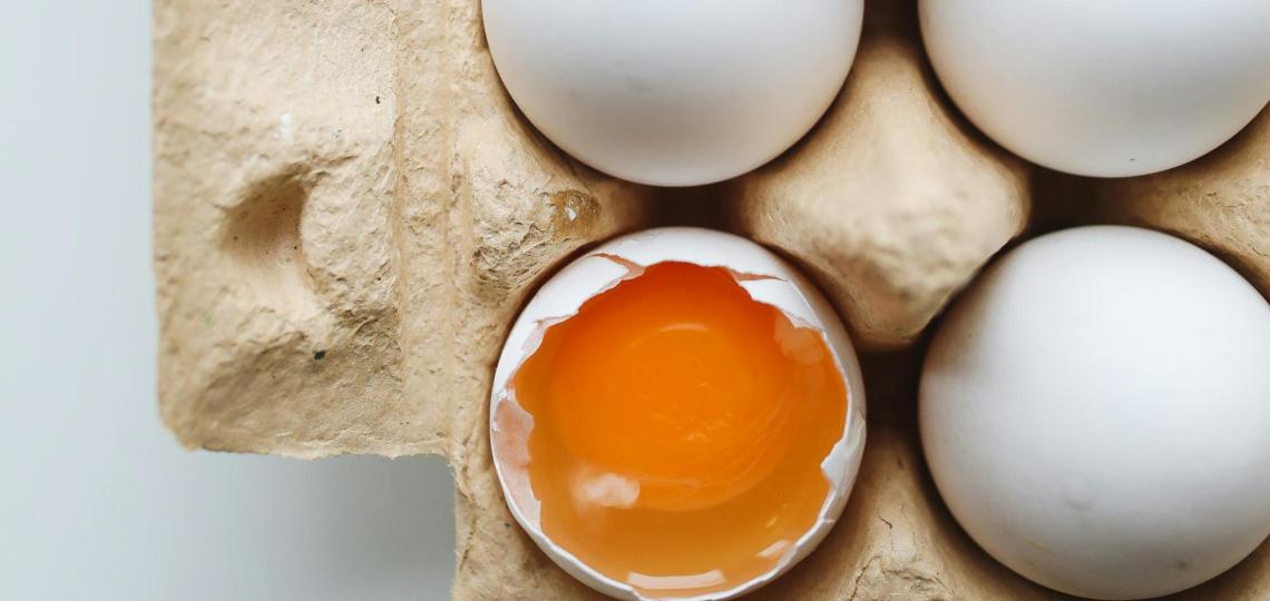 Photo of eggs in an open egg carton with one broken showing the yellow yolk.  