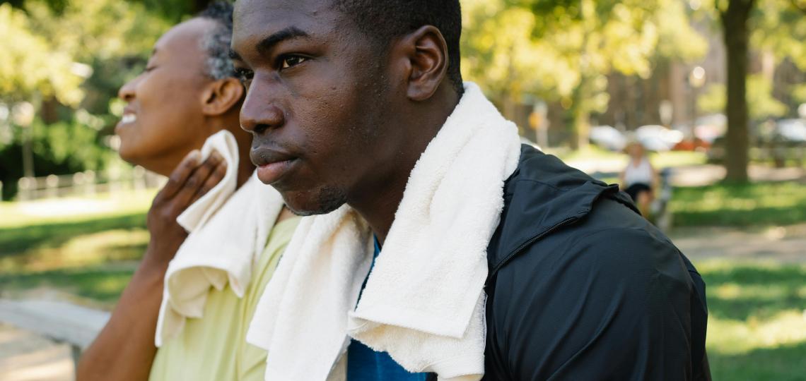 Two men sit outside in the heat, wearing towels around their neck to wipe their sweat. 