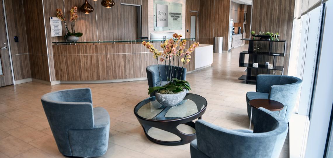 Modern clinic waiting area with blue chairs, glass coffee table with orchids, and a wood-paneled reception desk.