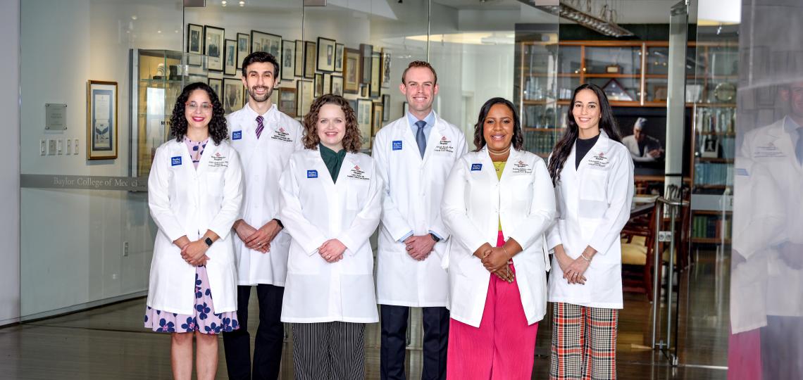 Six students in white coats smiling in a museum