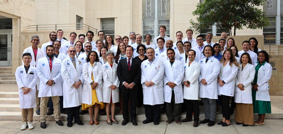 large group of doctors standing in front of a beige building, smiling