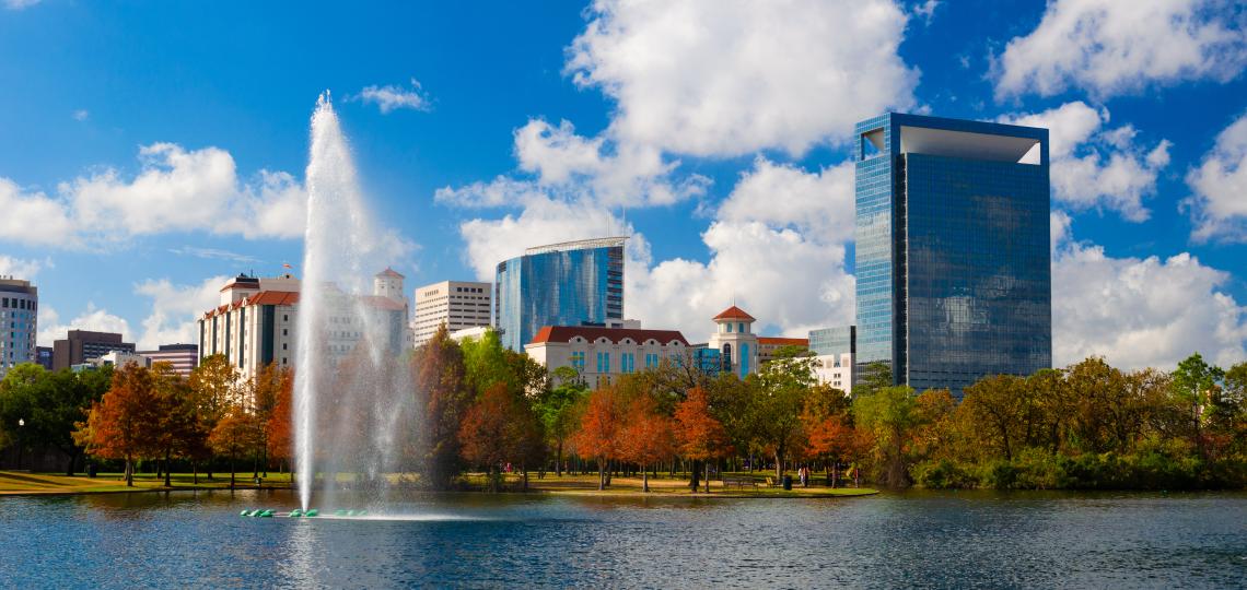 A view of the Texas Medical Center's skyline in the background of a large pond with a spout of water coming from a fountain. 