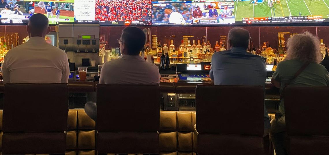 Four people sitting at bar watching sports games on TV