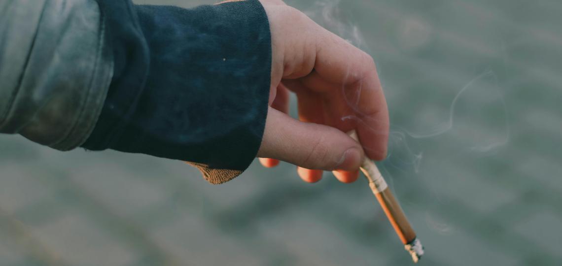 A close up photo of a hand holding a burning cigarette.