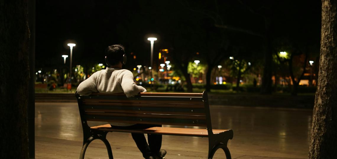 Photo of a man sitting on a bench overlooking a cityscape at night.