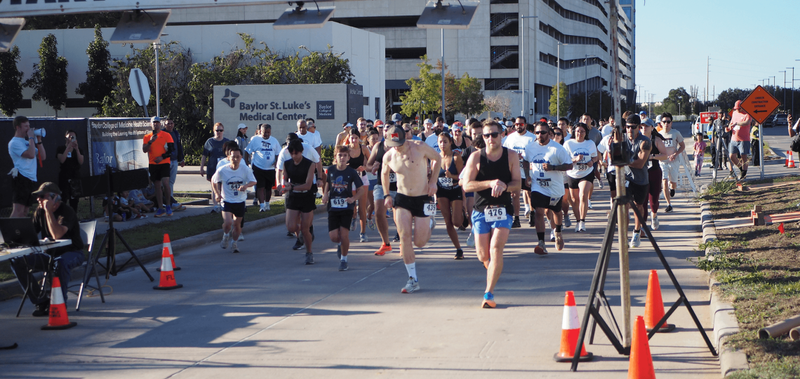 A large group of runners crossing a finish line during a 5K event.