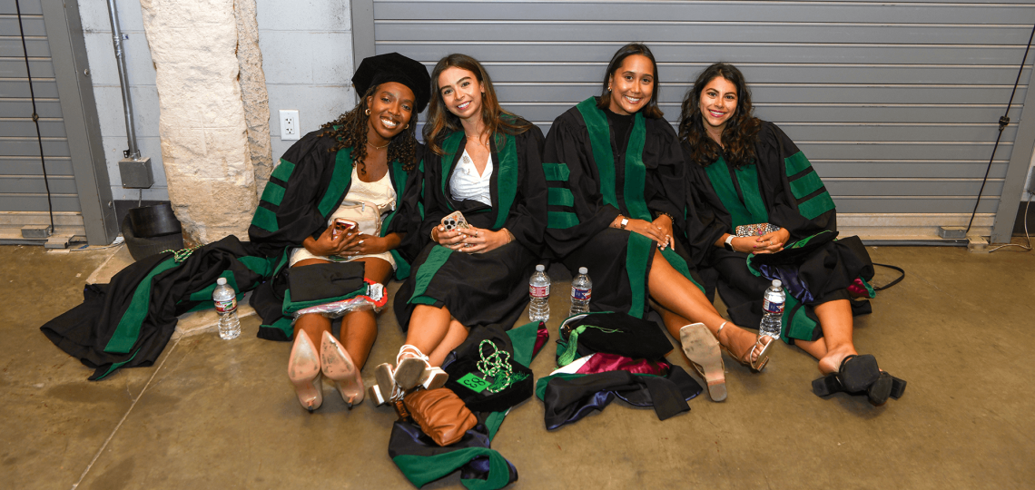 Four students in graduation robes taking a break while seated on the floor