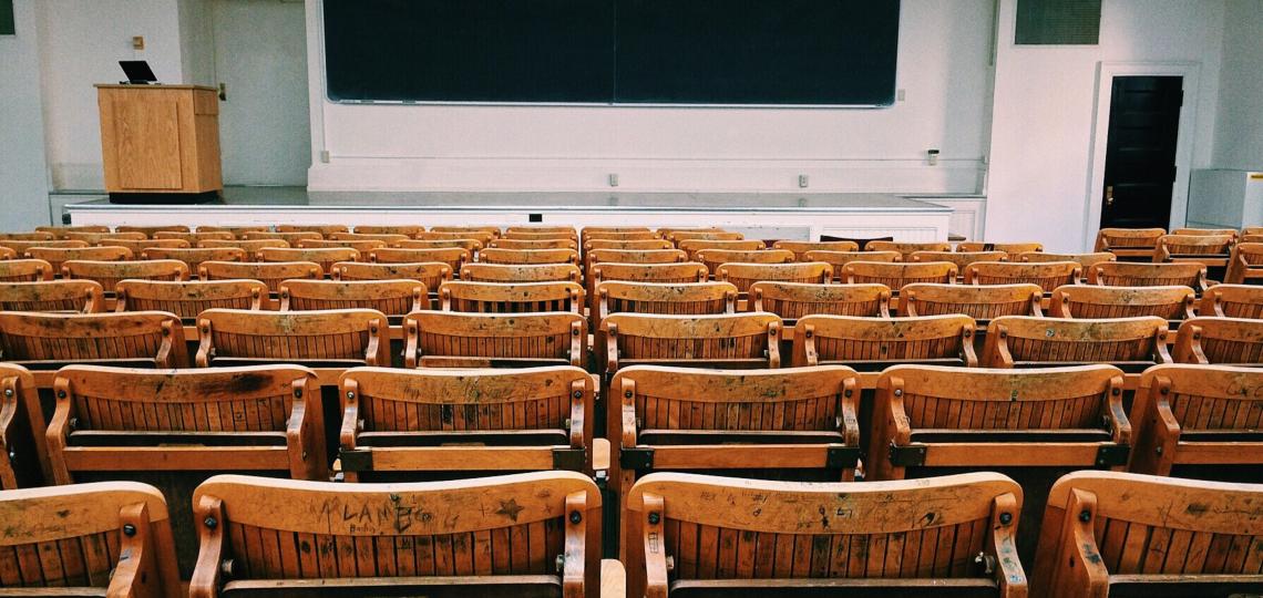 A photo of an empty college, auditorium style classroom with wooden chairs. 