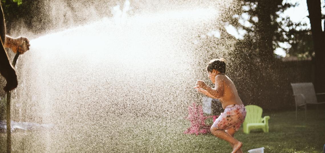 Photo of a child running through the spray of a water hose. 