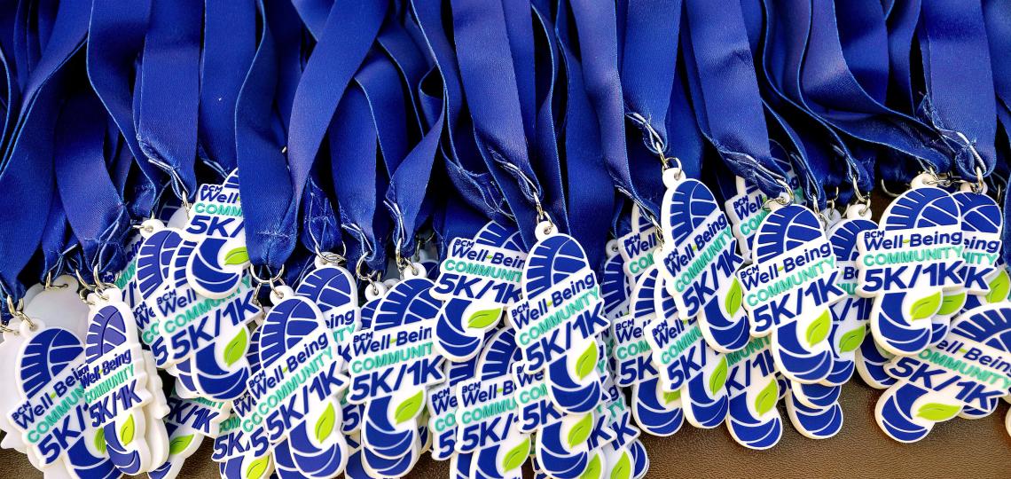 A collection of medals hanging from blue ribbons. The medals read BCM Well-Being Community 5K / 1K in shades of blue.