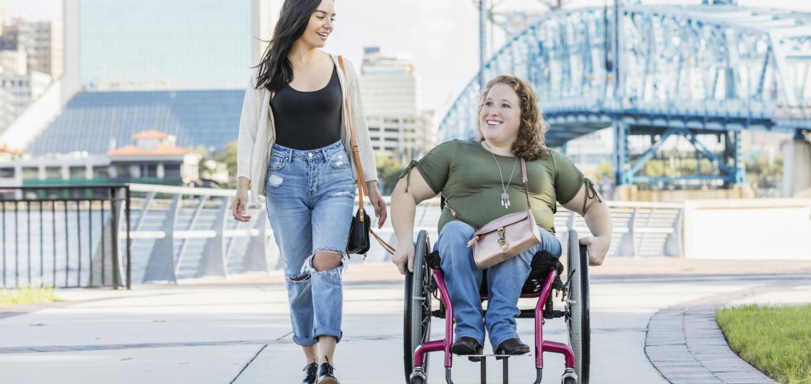 two women on a sidewalk, one in a wheelchair